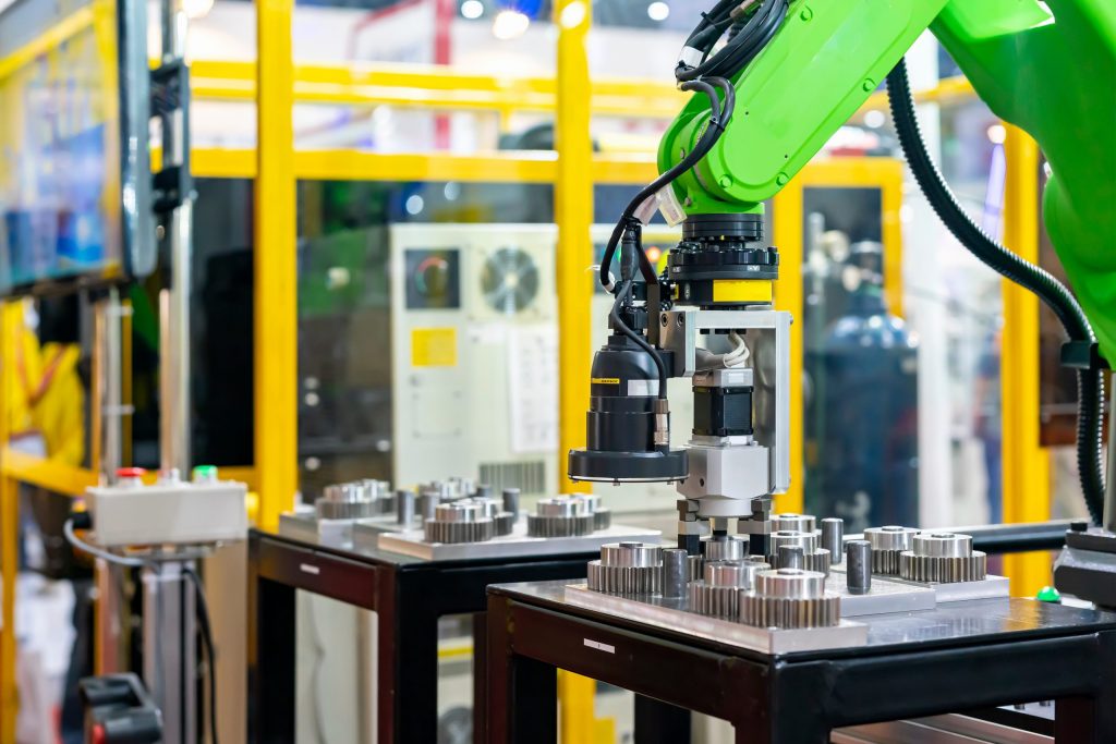 A robotic arm with a vision system inspects gears on a table in a factory floor environment