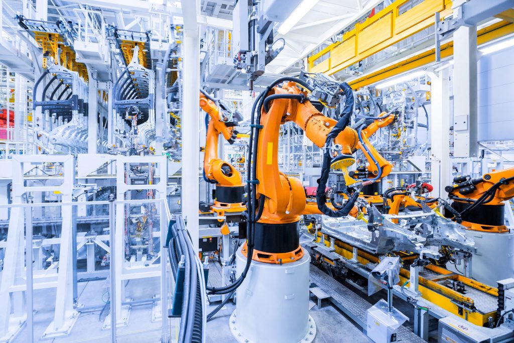 Orange robotic arms assembling vehicles in a big bright white factory