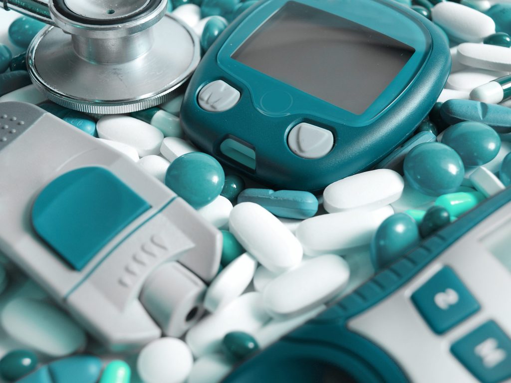 Consumer medical devices, a device for measuring blood sugar level, pills, and a stethoscope, all green and white.