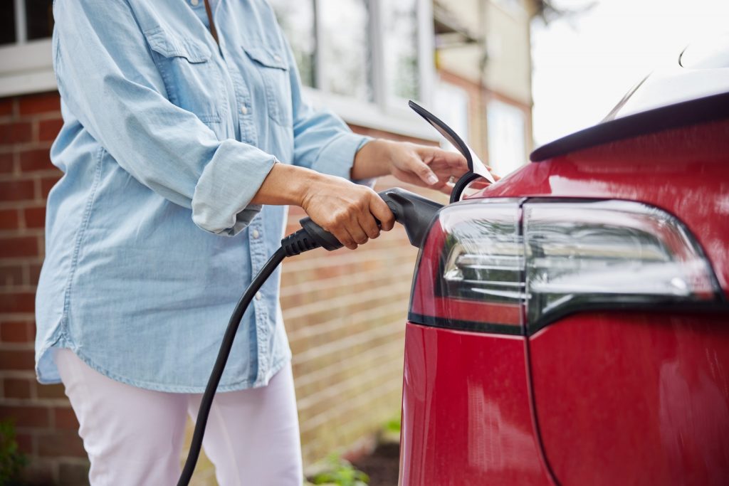 A woman attaching a charging cable to an environmentally friendly, zero emission electric car at home.
