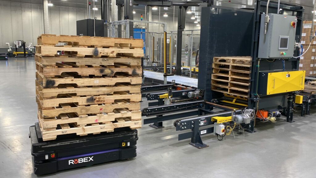 An AMR pallet loader moves a stack of empty pallets in a warehouse.