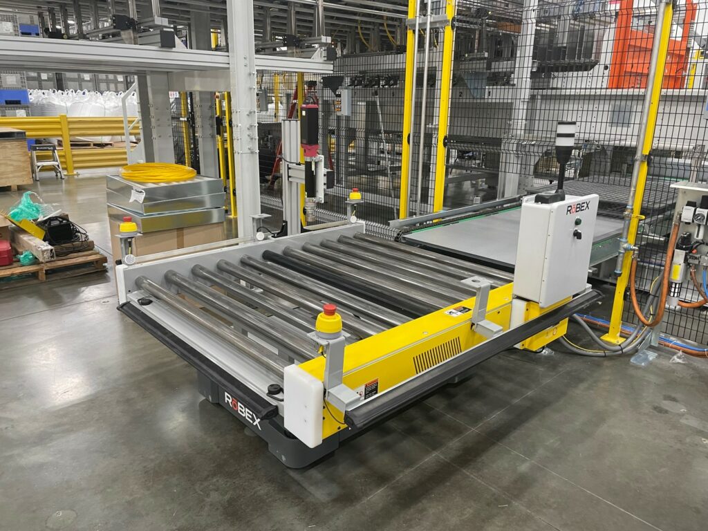 A RōBEX flex AMR transporter ready to receive a pallet in a warehouse.
