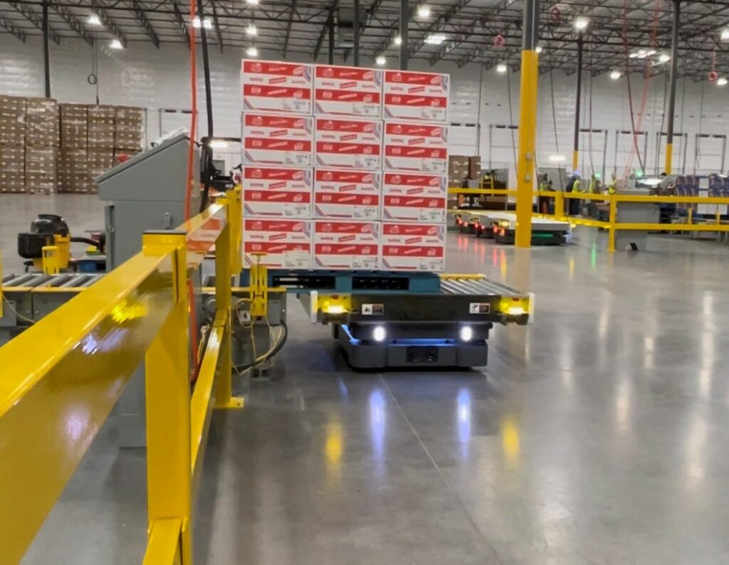 A yellow robot grabs a cardboard box from a conveyor.