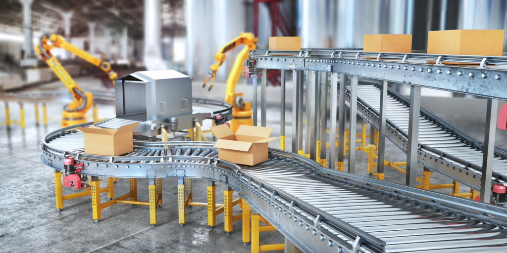 Cardboard boxes on a conveyor belt travel towards two yellow robotic arms.