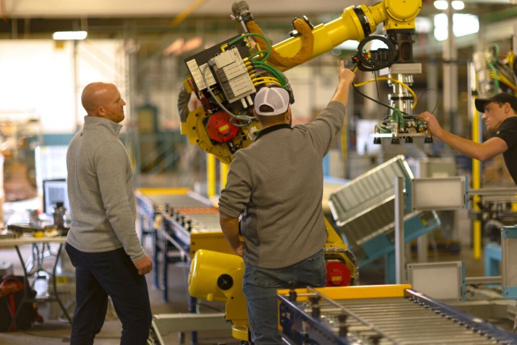 Engineers setting up a yellow industrial robotic arm used for an assembly line in a factory.