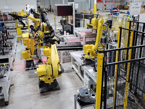 Yellow robotic arms work to assemble electric vehicle components.