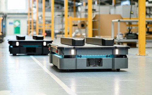 Two autonomous mobile robots move on a gray concrete floor.